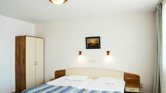 Hotellihuone, jossa on parivuode, yöpöytä ja vaatekaappi. (Tekoälyn luoma teksti)