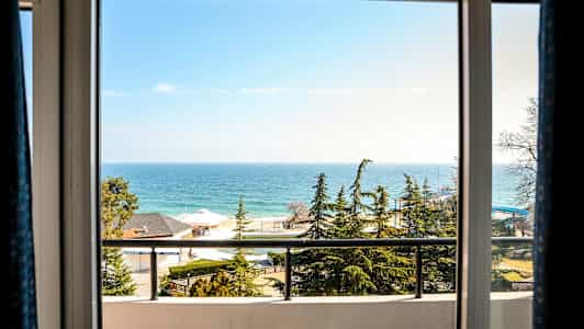 Näkymä ikkunasta näyttää meren, mäntyjä, taloja ja parveekkeen. (Tekoälyn luoma teksti)