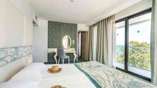 Hotellihuone, jossa on vaaleat kalusteet ja suuret ikkunat merinäköalalla. (Tekoälyn luoma teksti)