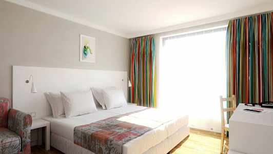 Hotellihuone, jossa on sänky, kirjoituspöytä ja värikkäät verhot. (Tekoälyn luoma teksti)