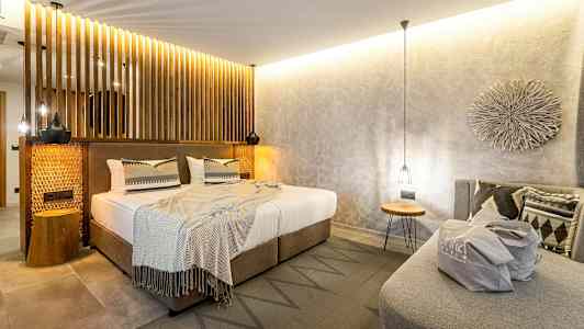 Makuuhuone modernilla sisustuksella, parivuode neutraaleilla vuodevaatteilla ja koristeellisilla tyynyillä sekä sohva, jonka päällä on laukku. (Tekoälyn luoma teksti)