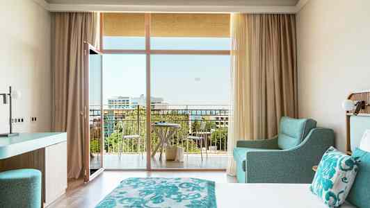 Hotellihuone, jossa parivuode, turkoosi sisustus ja parveke näköalalla. (Tekoälyn luoma teksti)