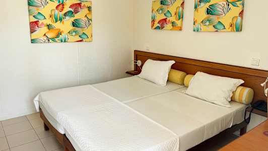 Hotellihuone, jossa kaksi erillistä sänkyä, valkoiset vuodevaatteet ja värikkäät maalaukset seinillä. (Tekoälyn luoma teksti)