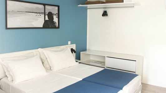 Hotellihuone, jossa kaksi erillistä vuodetta, valkoiset seinät ja sininen tehosteseinä. (Tekoälyn luoma teksti)