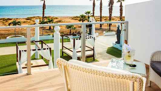 Näkymä parvekkeelta vehreään puutarhaan, jossa on sängyt katoksien alla ja taustalla meri. (Tekoälyn luoma teksti)