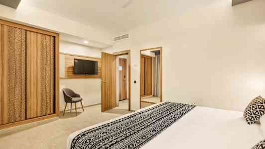 Hotellihuone, jossa suuri mustavalkoisella kuviolla koristeltu sänky, puukohdat huonekaluissa ja sisustuksessa, mukaan lukien vaatekaapit, ovet ja television kehys. (Tekoälyn luoma teksti)