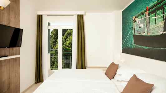 Hotellihuone, jossa on parivuode, seinään kiinnitetty TV ja suuri ikkuna vihreillä verhoilla. (Tekoälyn luoma teksti)