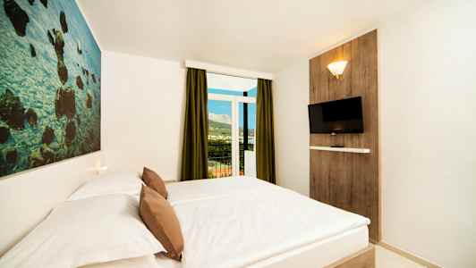 Hotellihuone, jossa on parivuode, seinäkoriste, seinälle kiinnitetty televisio ja parveke näkymällä. (Tekoälyn luoma teksti)