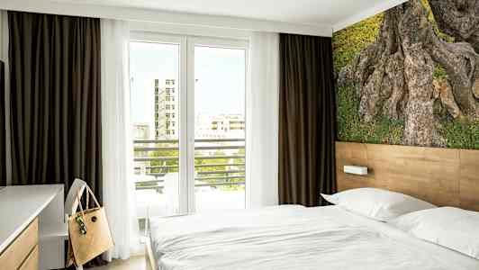 Hotellihuone, jossa sänky, työpöydän tuoli ja luontoaiheinen taulu seinällä. (Tekoälyn luoma teksti)