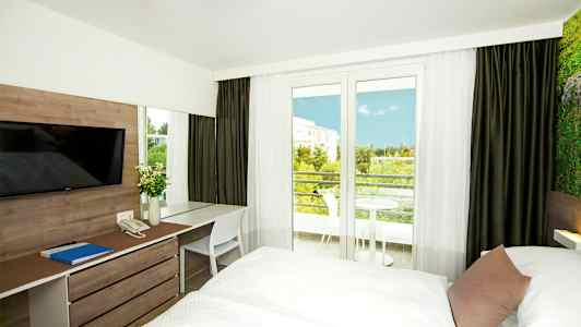Hotellihuone, jossa on kaksi vuodetta, työpöytä ja näkymä parvekkeelle ja vihreään maisemaan. (Tekoälyn luoma teksti)