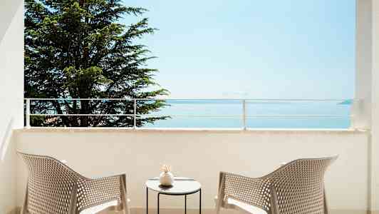 Näkymä parvekkeelta, jolla kaksi tuolia ja pöytä, kohti merta ja puuta. (Tekoälyn luoma teksti)