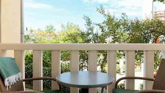 Kaksi tuolia ja pöytä parvekkeella, näkymä vihreään ympäristöön (Tekoälyn luoma teksti)