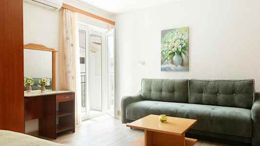 Valoisa sisätila, jossa vihreä sohva, pieni puupöytä ja peili kirjoituspöydän päällä. Seinällä on kukka-aiheinen maalaus. (Tekoälyn luoma teksti)