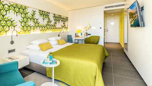 Hotellihuone, jossa on parivuode vihreällä päiväpeitteellä ja modernit kalusteet. (Tekoälyn luoma teksti)