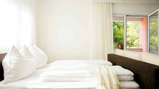 Valoisa huone, jossa sänky lähellä ikkunaa ja parveketta. (Tekoälyn luoma teksti)