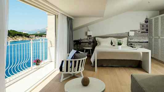 Hotellihuone, jossa on pedattu sänky, istuinalue ja parveke, josta näkyy merinäkymä. (Tekoälyn luoma teksti)