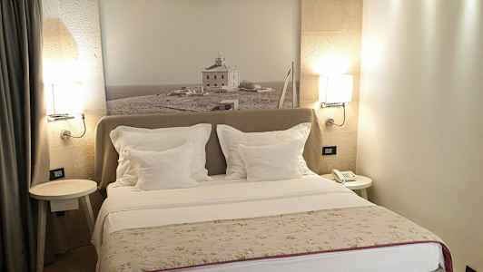 Hotellihuone, jossa parivuode, valkoiset tyynyt ja seinäkoriste, jossa valokuva maaseudulla olevasta talosta. (Tekoälyn luoma teksti)