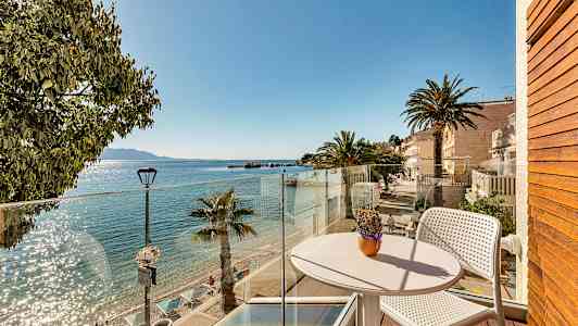 Näkymä parvekkeelta aurinkoiselle rannalle, jossa on palmuja ja kirkasta vettä. (Tekoälyn luoma teksti)