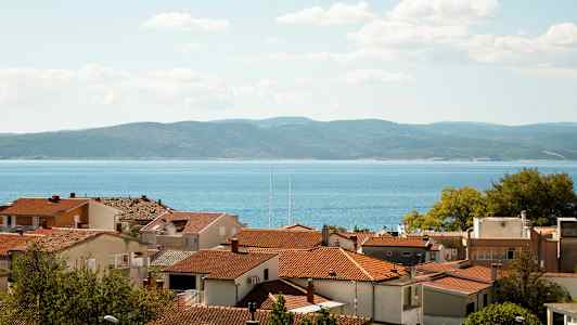 Punaisia kattotiiliä taloissa, taustalla meri ja mäet. (Tekoälyn luoma teksti)