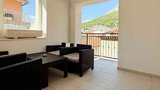 Terassi, josta näkymä kattojen ja luonnon yli, varustettu tummilla rottinkituoleilla ja pöydällä. (Tekoälyn luoma teksti)