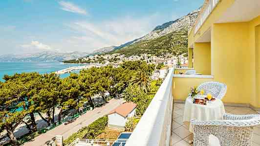 Näkymä keltaisen rakennuksen parvekkeelta kaupungin yli meren äärellä ja ympäröiviin vuoriin. (Tekoälyn luoma teksti)