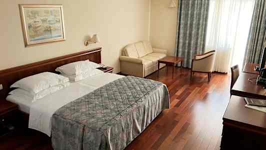 Hotellihuone, jossa on parivuode, sohva, puupöytä ja tuoleja sekä työpöytä televisiolla. (Tekoälyn luoma teksti)