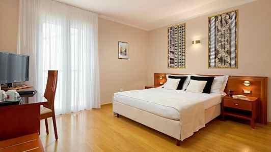 Hotellihuone, jossa on parivuode, kirjoituspöytä ja tuoli sekä televisio. (Tekoälyn luoma teksti)