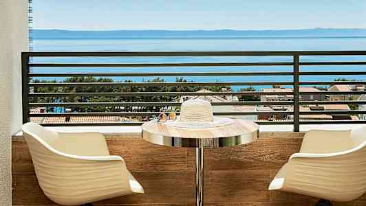 Näkymä merelle parvekkeelta, jossa istuimia ja pöytä. (Tekoälyn luoma teksti)