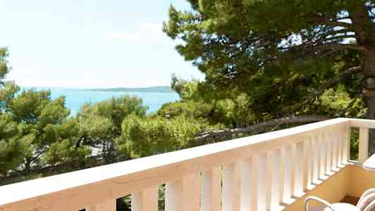 Näkymä parvekkeelta, jossa on valkoinen kaide, kohti puita ja merta. (Tekoälyn luoma teksti)