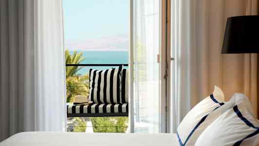 Sänky, jossa valkoiset ja siniset lakanat, vieressä parveke näkymällä merelle. (Tekoälyn luoma teksti)