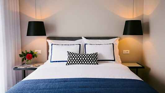 Kuva pedatusta sängystä, jossa on koristeellisia tyynyjä ja riippuvia valaisimia. (Tekoälyn luoma teksti)