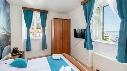 Hotellihuone, jossa on parivuode, siniset verhot ja näkymä satamaan ikkunan ulkopuolella. (Tekoälyn luoma teksti)