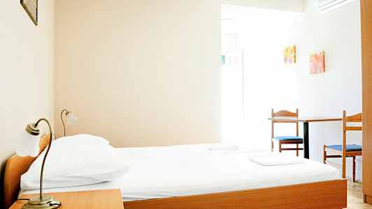 Yksinkertainen hotellihuone, jossa on puinen sänky, yöpöytä ja pöytä kahdella tuolilla. (Tekoälyn luoma teksti)