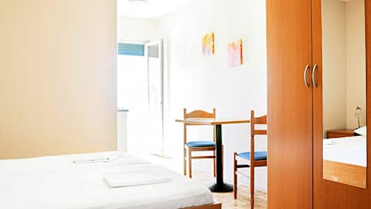 Hotellihuone, jossa kaksi erillistä vuodetta, pöytä ja kaksi tuolia sekä vaatekaappi. (Tekoälyn luoma teksti)