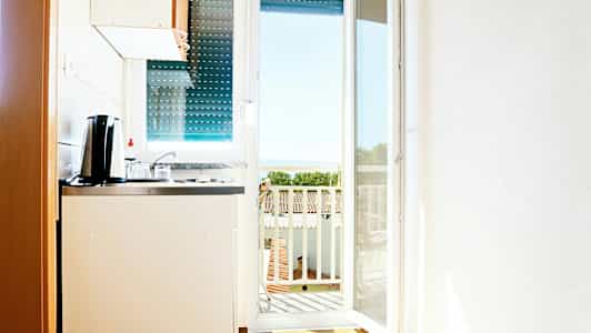 Pieni keittiö, josta on näkymä parvekkeelle ja taustalla näkyy meri. (Tekoälyn luoma teksti)
