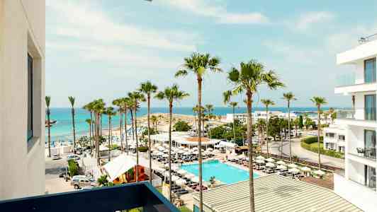 Näkymä rannalle, missä palmuja, uima-allas ja valkoinen rakennus meren äärellä. (Tekoälyn luoma teksti)