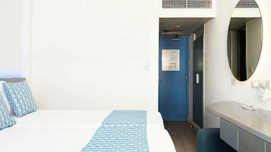 Hotellihuone, jossa kaksi vuodetta, sinisiä yksityiskohtia ja kirjoituspöytä. (Tekoälyn luoma teksti)