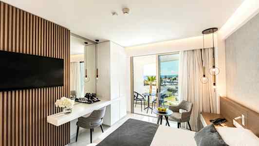 Moderni hotellihuone, jossa on parivuode, pöytä ja tuolit sekä merinäköala parvekkeelta. (Tekoälyn luoma teksti)