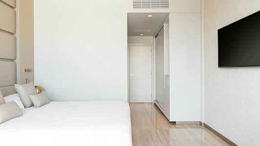 Moderni hotellihuone, jossa on suuri sänky, valkoinen seinä, ovi ja seinälle asennettu televisio. (Tekoälyn luoma teksti)