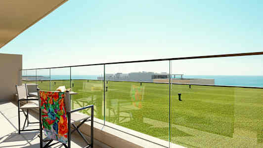 Terassi, jossa lasikaide, tuolit ja näkymä vihreille nurmikoille ja merelle. (Tekoälyn luoma teksti)