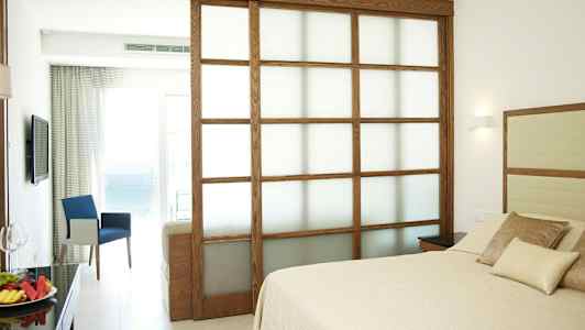 Hotellihuone, jossa on sänky ja istuinryhmä sekä näkymä merelle. (Tekoälyn luoma teksti)