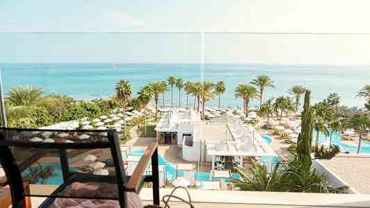 Näköala merelle, hotellialue palmujen ja altaiden kanssa sekä tuoli etualalla. (Tekoälyn luoma teksti)