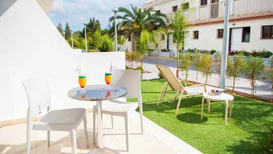 Terassikalusteet, joilla on kaksi värikästä juomaa, ja taustalla näkyy nurmikko aurinkotuolilla. (Tekoälyn luoma teksti)