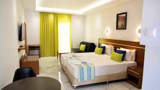 Hotellihuone, jossa on kaksi pedattua sänkyä, värikkäitä tyynyjä, pieni istuinryhmä ja limenvihreät verhot. (Tekoälyn luoma teksti)