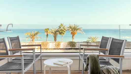 Näköala terassilta, jossa on tuoleja, pöytä ja taustalla näkyy meri. (Tekoälyn luoma teksti)