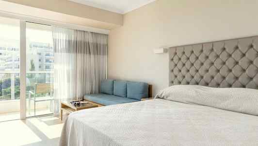 Hotellihuone, jossa sänky, sininen sohva ja parveke. (Tekoälyn luoma teksti)