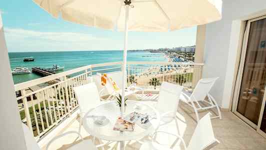 Parveke, jossa on pöytä ja tuolit, näkymä rannalle ja merelle. (Tekoälyn luoma teksti)