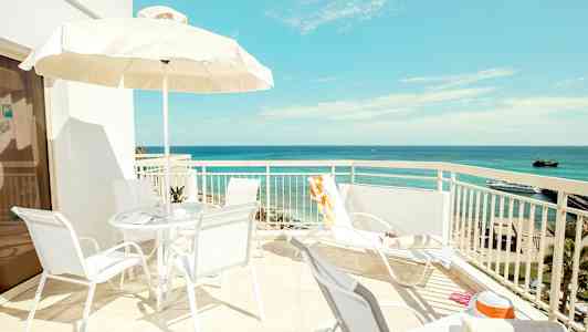 Aurinkoinen terassi, jolta on näkymä merelle, tuolit ja varjo. (Tekoälyn luoma teksti)