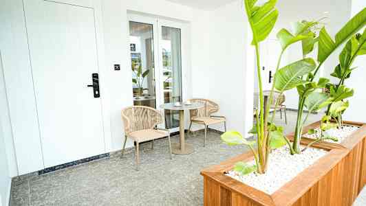 Terassi, jossa kaksi tuolia ja pöytä, ympäröitynä vihreillä kasveilla. (Tekoälyn luoma teksti)