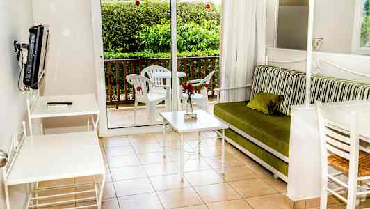 Olohuone, jossa vihreä sohva, valkoinen pöytä ja tuolit sekä parveke kalusteineen. (Tekoälyn luoma teksti)